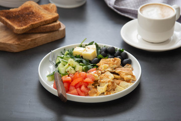 Omelette with fresh vegetables: rocket, tomatoes, cucumber, olives, cheese. Dark background. Top view.