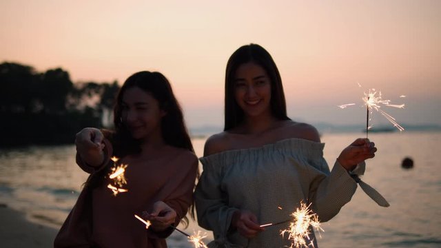 Asian teenage girl playing firework beautiful light sparkle at seaside in beach summer. Young female happy festival and anniversary celebration. Young women is travel blogger.