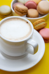 Cup of coffee and macaroons on colorfu lyellow background.