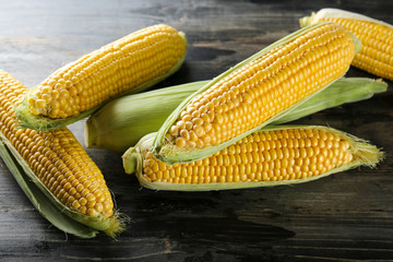 Cobs of ripe raw corn laid on dark wood textured table. Healthy summer food concept. Fresh uncooked corncob. Clean eating habits. Background, top view, close up, flat lay, copy space.