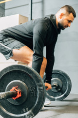 Fit young man in sportswear preparing to lift weights during an workout session in a gym. Fitness sport or healthy lifestyle concept.