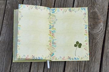 Blank notepad pages with green, floral pattern. Dried four-leaf clover plan