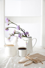 Festive table decoration for Easter. Coffee, milk jug and a bouquet of blue flowers in jug, as well as a bag with a gift in the shape of an Easter hare.