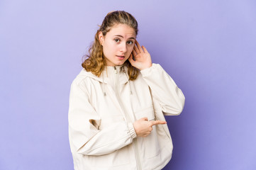 Obraz premium Young caucasian woman on purple background trying to listening a gossip.