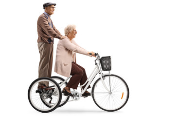 Naklejka premium Senior woman riding a tricycle and a senior man standing behindd and holding onto her