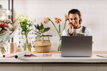 Young businesswoman talking on cell phone in flower shop. Female florist standing at shop counter.