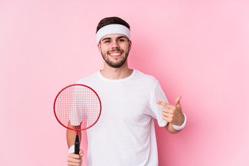 Young caucasian man playing badminton isolated person pointing by hand to a shirt copy space, proud and confident