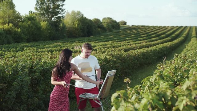 Cheerful artists' couple creatives a landscape and talks in bush field