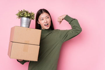 Young chinese woman holding boxes isolated raising fist after a victory, winner concept.