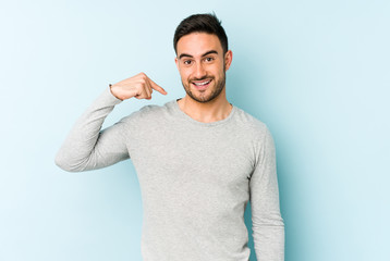 Young caucasian man isolated on blue background person pointing by hand to a shirt copy space, proud and confident