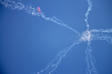 Star-shaped smoke jets and a tiny skydiver on a high altitude in a blue sky.