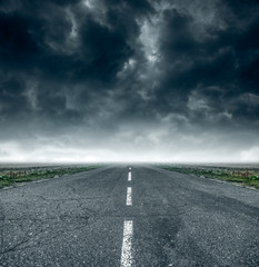 Fototapeta premium Road into the distance against a cloudy dark sky.