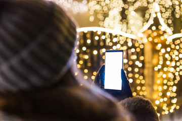 Woman using empty screen smart phone in front of house with new year christmas decoration lamps.