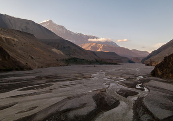 The wide river bed of the Kali Gandaki valley surrounded by the barren snow covered Himalayan mountains of the cold desert landscape of Upper Mustang on the Annapurna Circuit trail in Nepal.