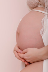 Close-up of unrecognizable pregnant woman with hands at pastel pink background.