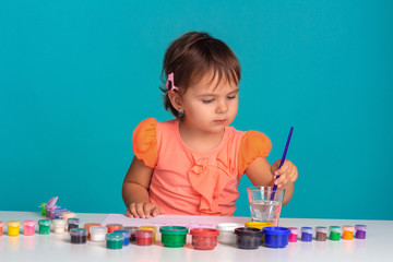 Cute little child girl drawing paints at the table. On blue background. Studio shoot.