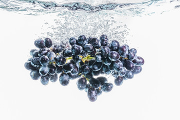 Bunch of red grapes splashing into crystal clear water on withe background
