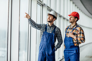 Two builders construction stand by the big windows and hang out at work.