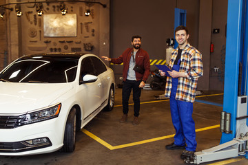 Full Length shot of young mechanic with clipboard looking at the camera while customer standing on the background with a car