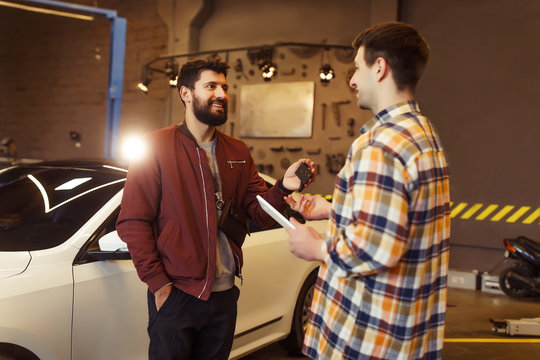bearded mand and mechanic standing in workshop and talking together