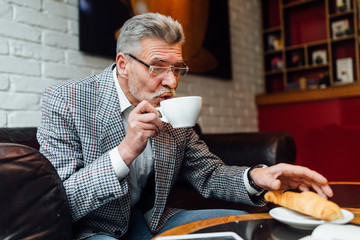 Middle-aged man in trendy suit have a nice weekend with cup of coffee and croissant