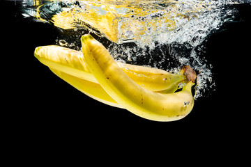 Fresh bananas splashing into water on black background.