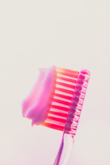 Pink plastic toothbrush with a white toothpaste on an isolated background.