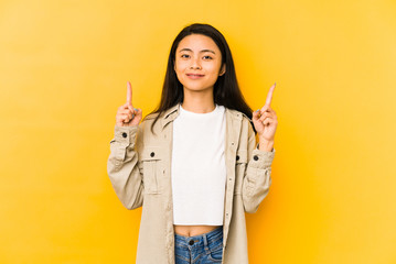 Young chinese woman isolated on a yellow background indicates with both fore fingers up showing a...