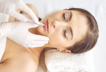 Obraz na płótnie Canvas Beautician doing beauty procedure with syringe to face of young brunette woman. Cosmetic medicine and surgery, beauty injections