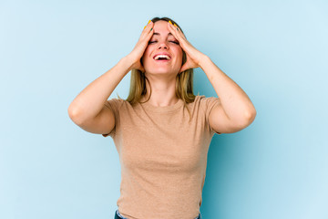 Young caucasian woman isolated on blue background laughs joyfully keeping hands on head. Happiness concept.