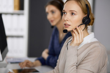 Businesswoman talking by headset while sitting in office. Call center and diverse people group in...