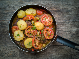 Meat with broth and vegetables in frying pan isolated on rustic wooden background. Flat lay.