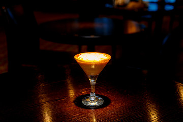 Coffee cocktail with white foam on the counter of a dark bar.