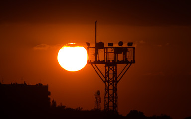 A silhouette of an industrial tower with a background of a sun low above the horizon.