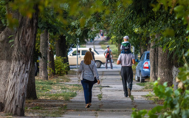 People walking along the street surrounded by green leafed trees.s