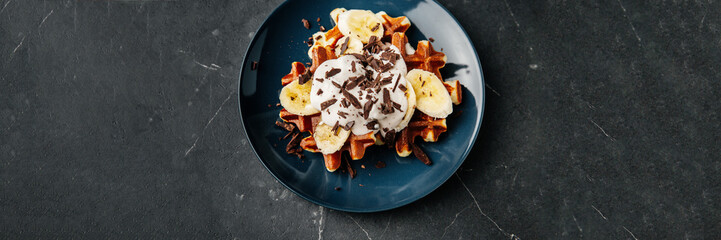 Viennese waffles on a plate, with a crumb of chocolate and slices of banana on a dark textured background.