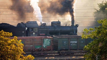 An old vintage train releases lots of smoke and steam into the air.