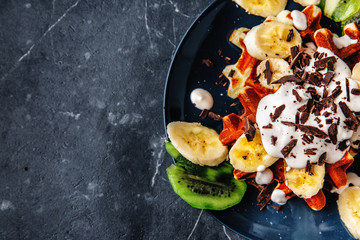Viennese waffles on a plate, with cream sprinkled with a crumb of chocolate, slices of banana and kiwi on a dark textured background.