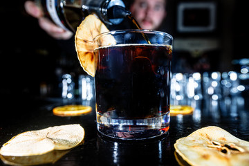 A cocktail with whiskey or cognac or Cola in a highball glass is on the counter of a dark bar.