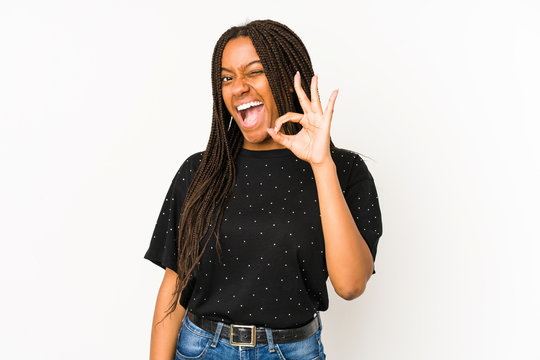 Young african american woman isolated on white background winks an eye and holds an okay gesture with hand.