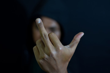Young man showing middle finger, criminal type of person on dark black background. selective focus on finger