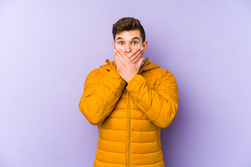 Young man isolated on purple background shocked covering mouth with hands.