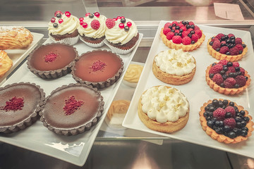 cakes with different fillings and colored glaze, decorated with fruits and berries behind the shop window