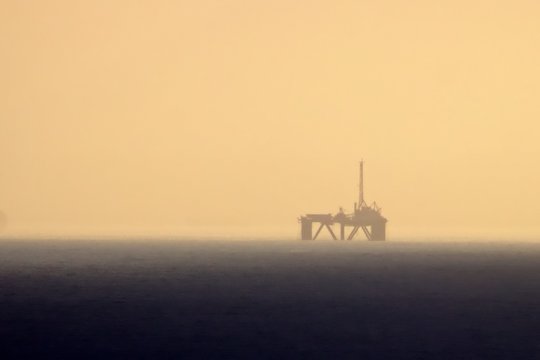 The gas rig out at sea through a hazy sky as the sun sets over the ocean in Mosselbay, South Africa