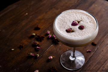 Sauer cocktail in a wide cocktail glass with dried rose stands on the counter of a dark bar.