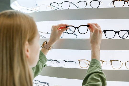 woman pick a eyeglasses from shelf in optics store - Powered by Adobe