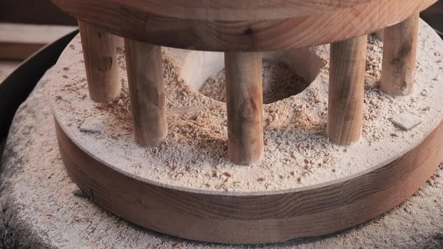 The ancient quern stone hand mill with grain. The man grinds the grain into flour with the help of a millstone. Old grinding stones turned by human hands. Miller pours grain into a stone millstone.