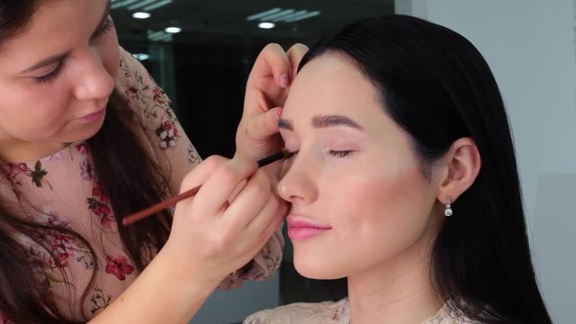 Make-up artist makes up the model's eyes, puts shadows on the eyelid, in a professional Studio. Concept of professional eye makeup, make-up, video techniques for applying eye shadows.