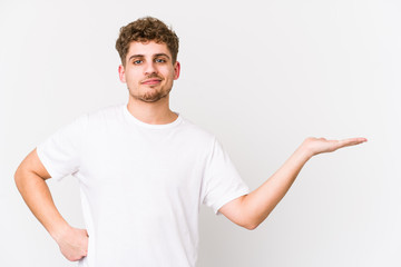 Young blond curly hair caucasian man isolated showing a copy space on a palm and holding another hand on waist.