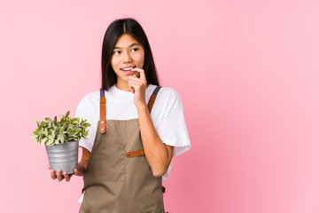 Young chinese gardener woman holding a plant isolated relaxed thinking about something looking at a copy space.